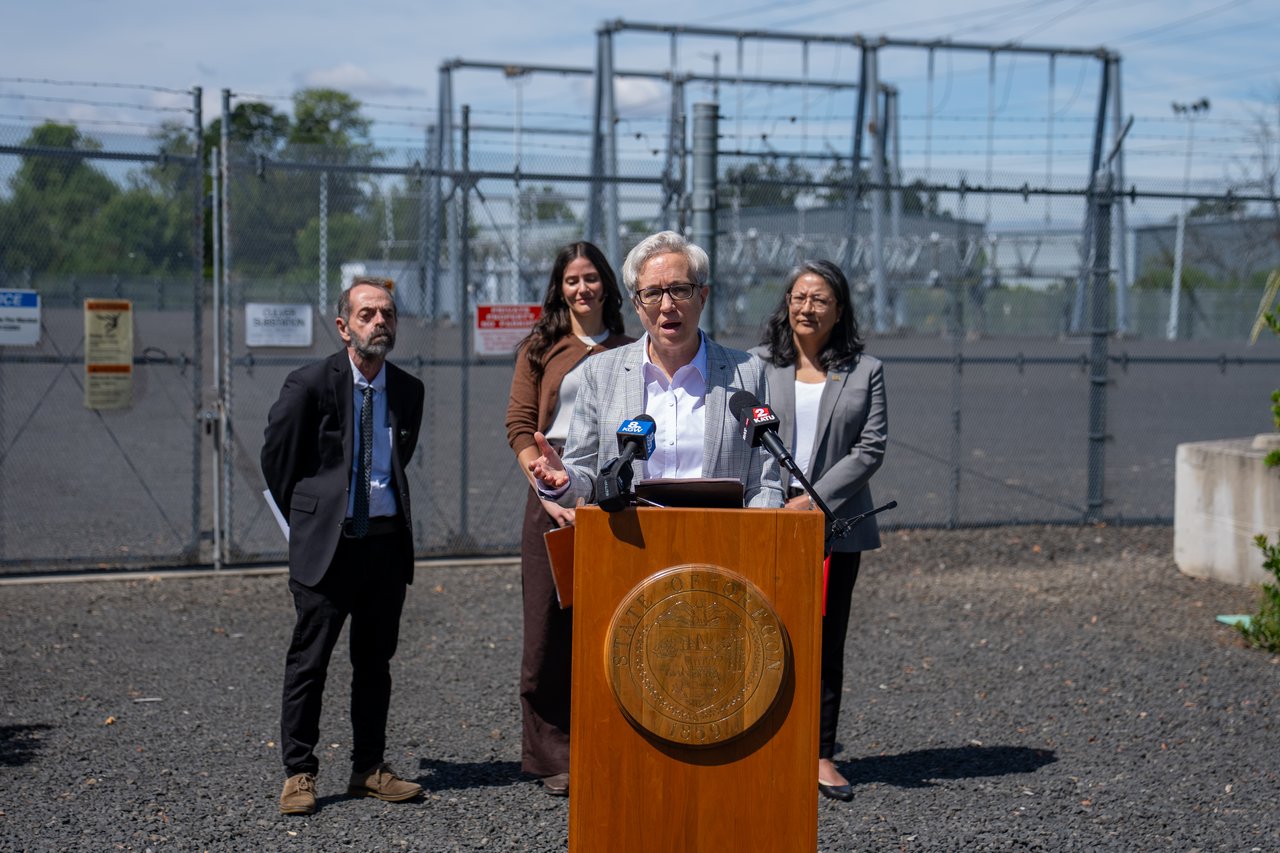 Oregon officials at a podium near electrical infrastructure
